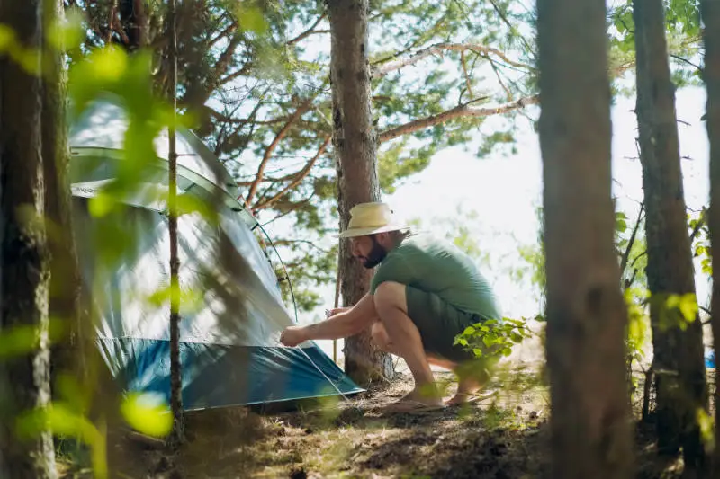 Zomers geklede man zet een tentje op in een bos.
